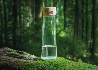 Une bouteille en verre avec bouchon en liège personnalisé avec logo posée sur une branche d'arbre dans un décor naturel